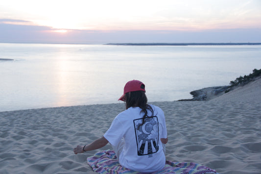 Assise sur la plage, porte le t-shirt Wink face à l'océan